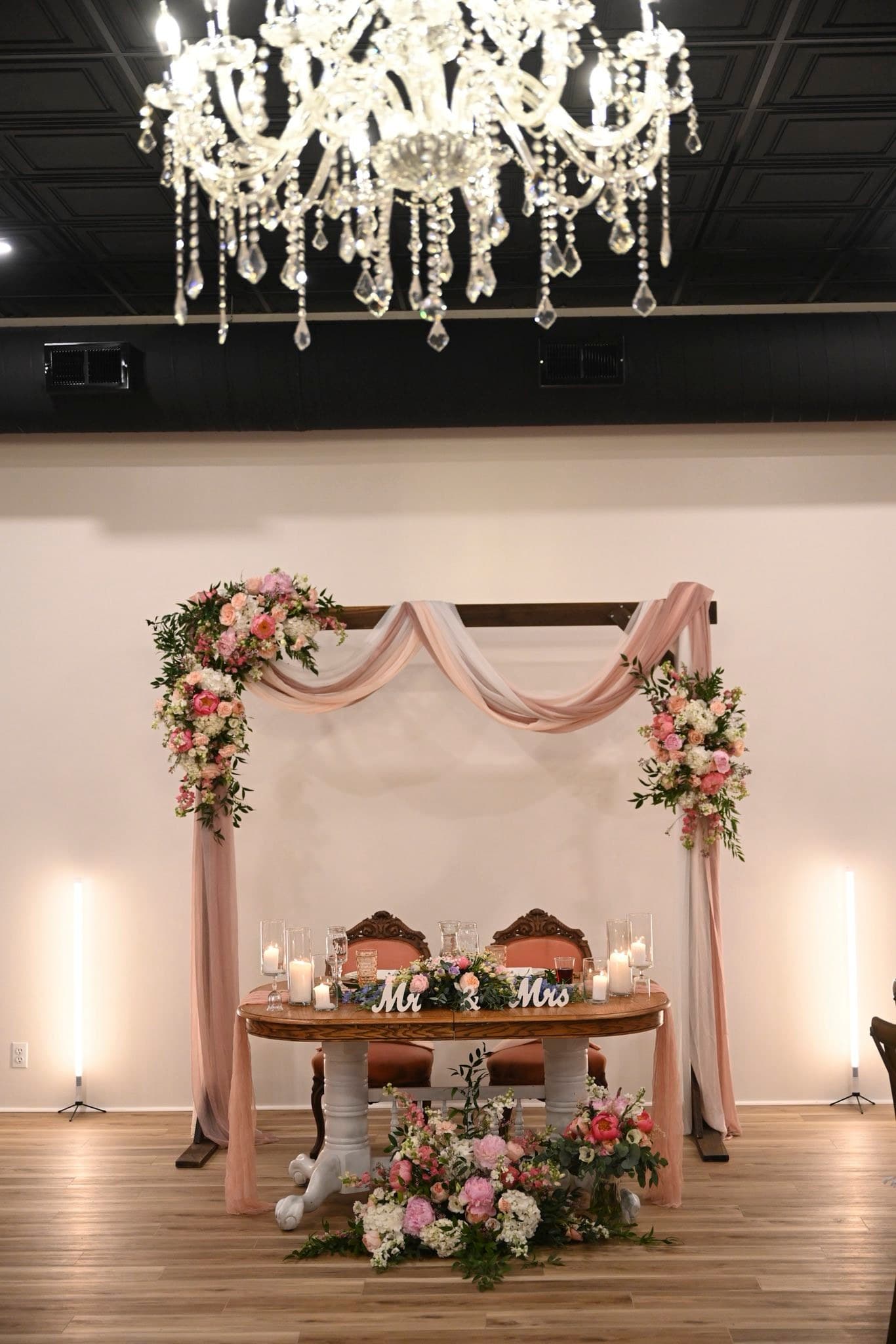 Blush draped ceremony arch and sweetheart table beneath a crystal chandelier at Becker Hill