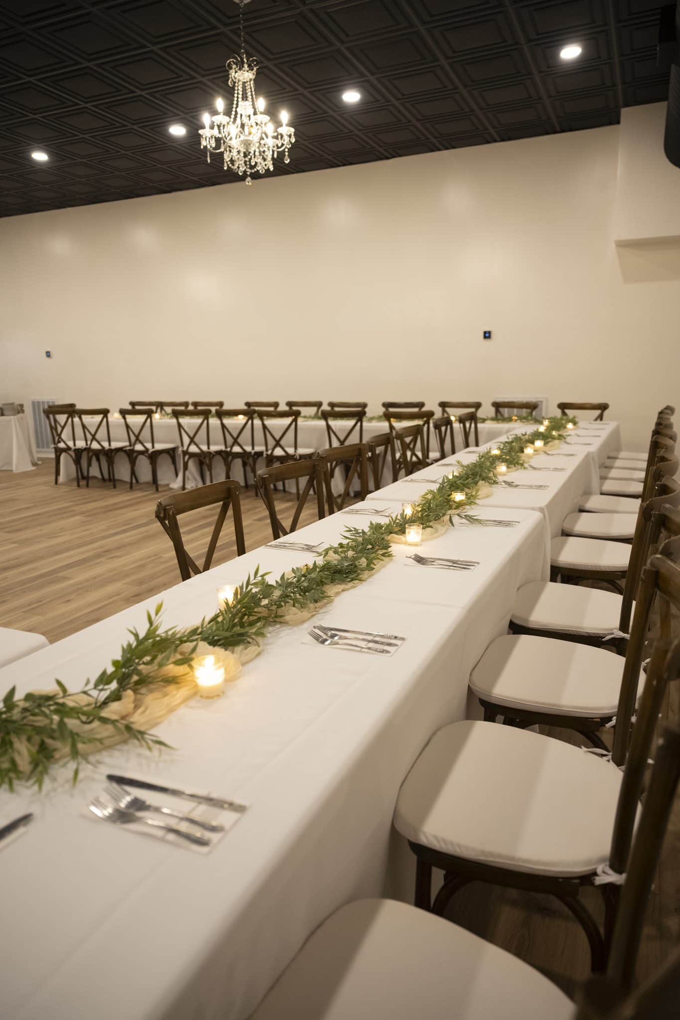 Long banquet table with a greenery runner and candles under a crystal chandelier in the Becker Hill reception hall