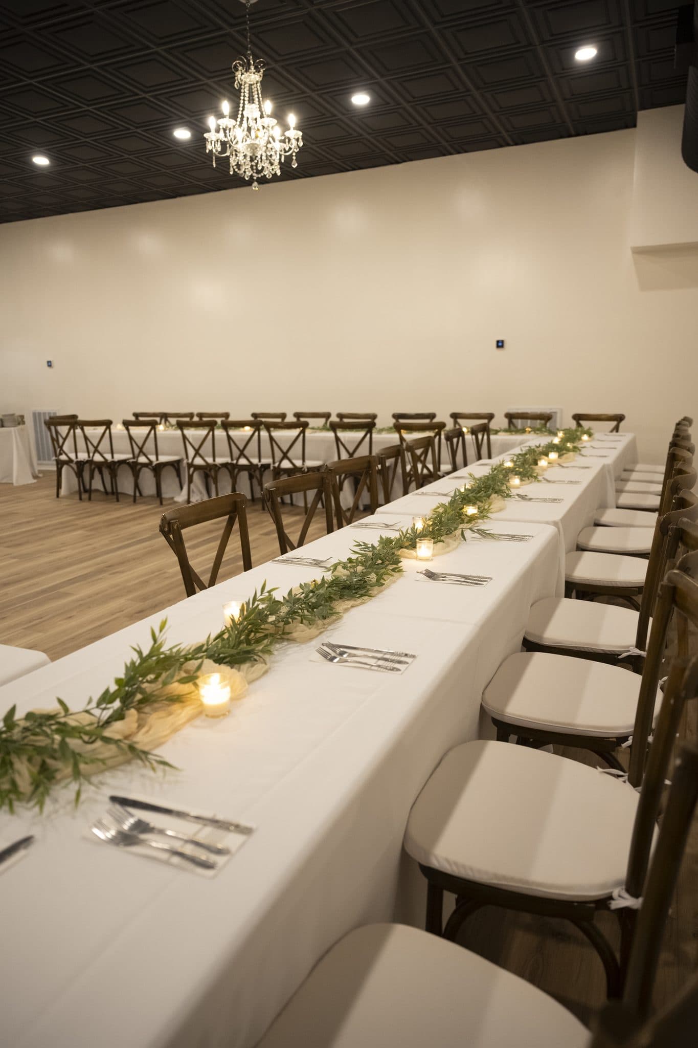 Long banquet table with a greenery runner and candles under a crystal chandelier in the Becker Hill reception hall