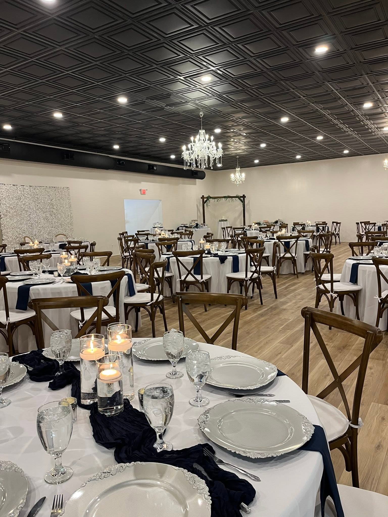 Becker Hill reception hall set with navy table runners, crystal chandeliers, and a ceremony arch in the background