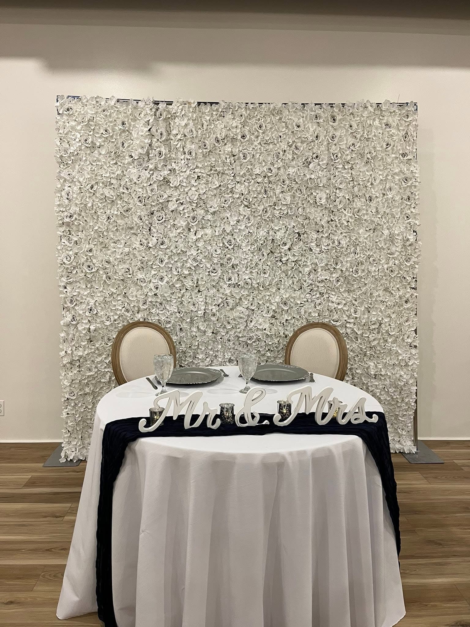 Mr and Mrs sweetheart table in front of a white flower wall at Becker Hill