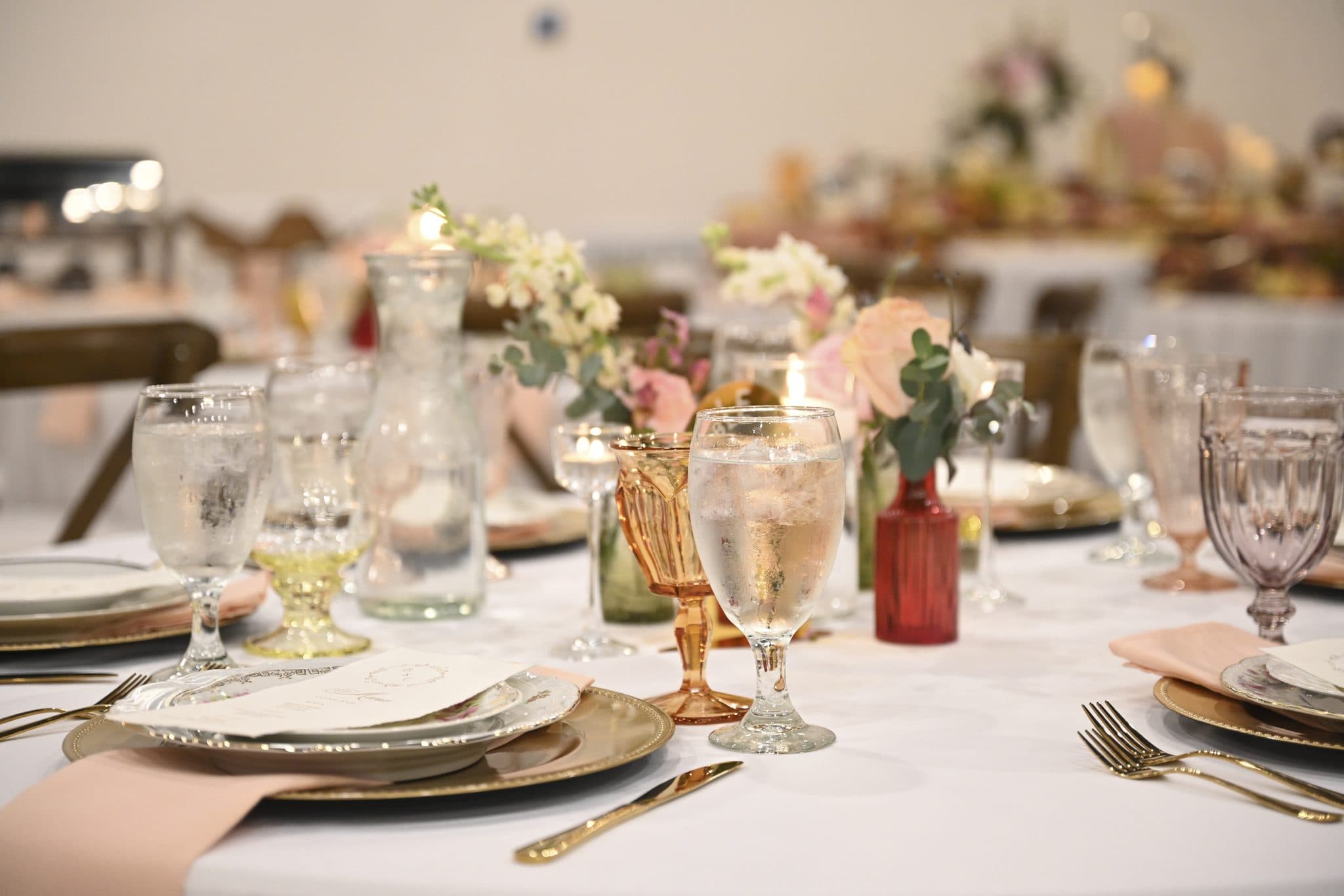 Close table setting with gold chargers, coloured glassware, and fresh florals at a Becker Hill reception