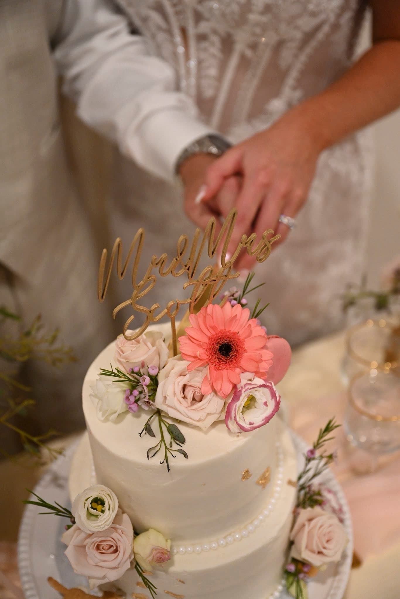Close-up of a couple cutting their floral wedding cake with a Mr and Mrs cake topper at Becker Hill